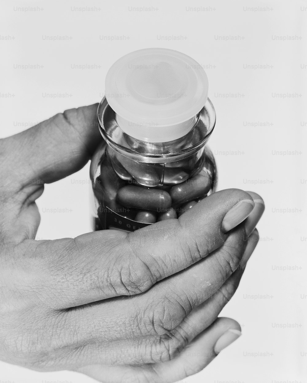 a black and white photo of two hands holding a jar of pills