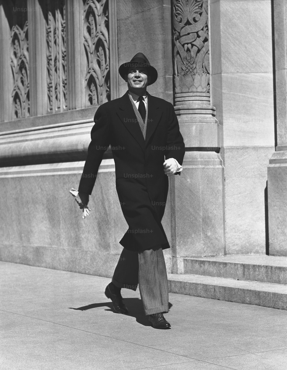 a man in a suit and hat walking down a sidewalk