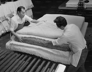 two men working on a mattress in a factory