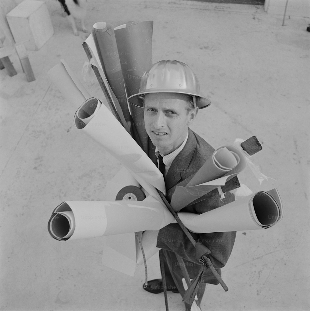 a black and white photo of a man in a hard hat holding a bunch of