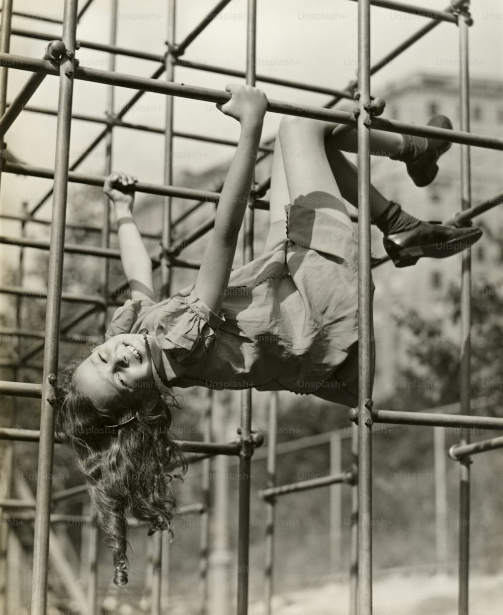 UNITED STATES - CIRCA 1950s:  Child girl hanging upside down on jungle gym.