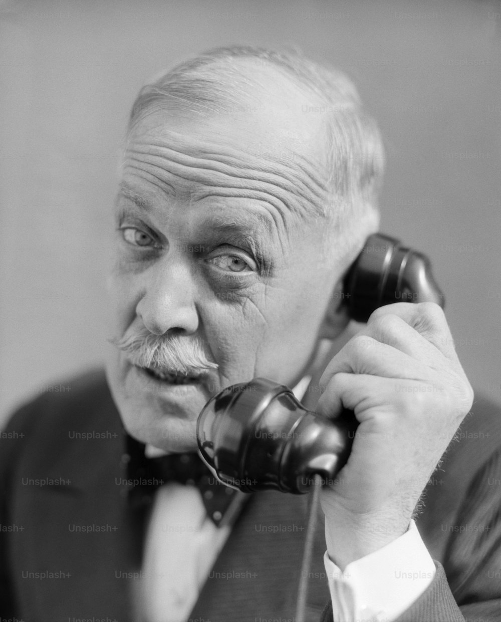 UNITED STATES - Circa 1930s:  Elderly Man Head Shot On Phone Worried Concerned Expression Moustache Wrinkled Brow Forehead Bowtie Distinguished Businessman.