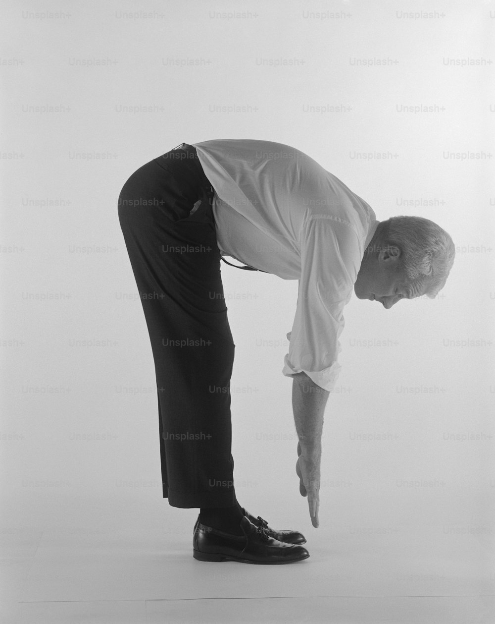 a man in a white shirt and black pants bending over