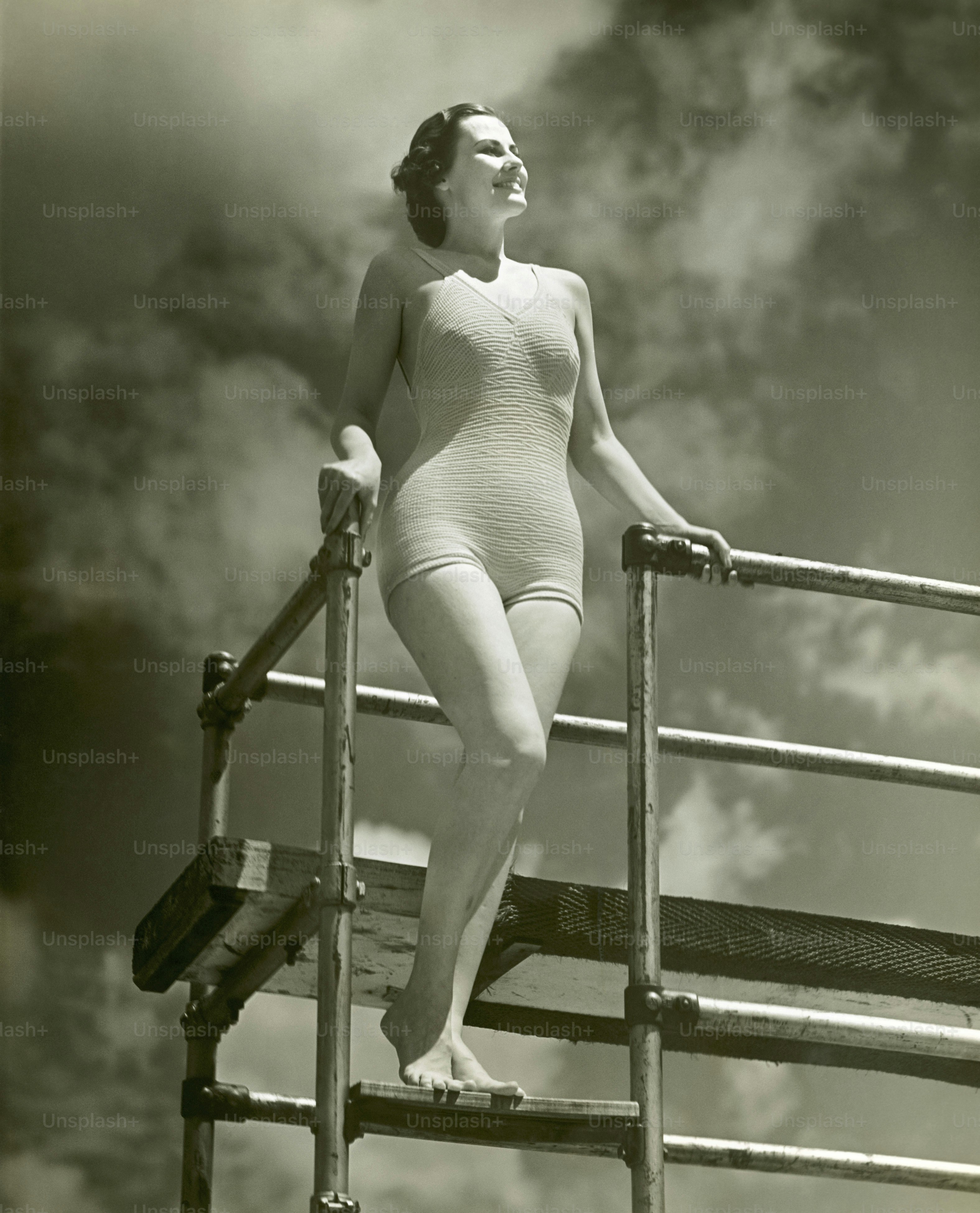 ÉTATS-UNIS - Circa 1950s : Femme en maillot de bain sur une échelle de plongeoir