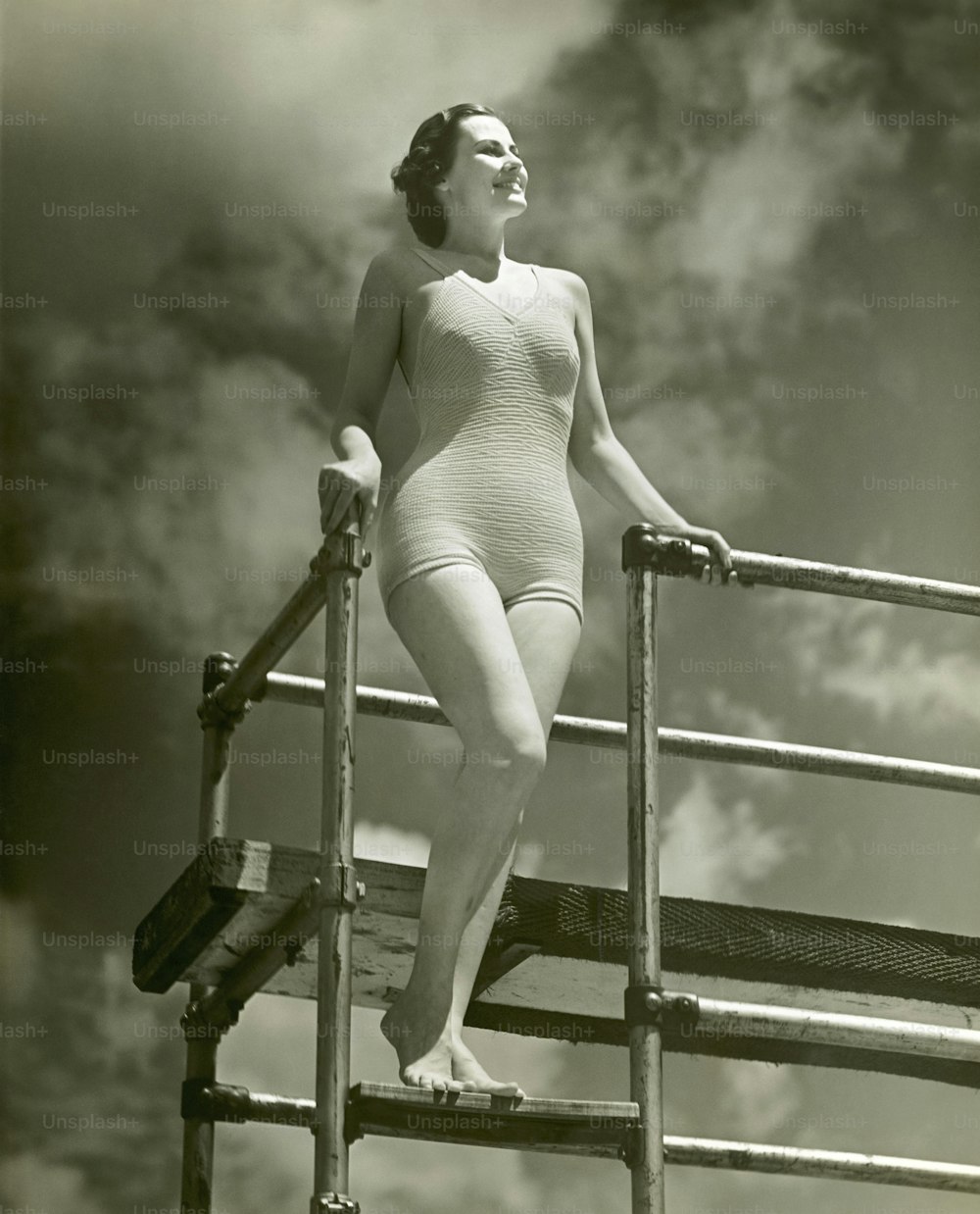 UNITED STATES - CIRCA 1950s:  Woman in bathing suit on diving board ladder.