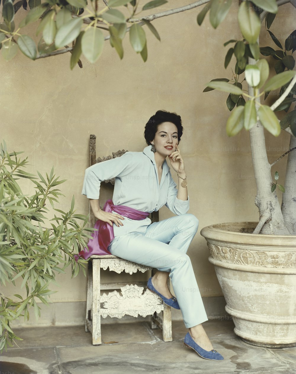 a woman sitting on a chair next to a potted plant