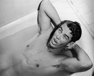Un hombre acostado en una bañera con las manos detrás de la cabeza, alrededor de 1955.