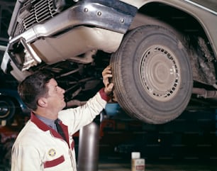 VEREINIGTE STAATEN - CIRCA 1960er Jahre: Automechaniker Mann in Tankstelle, überprüft Profil auf Gummireifen, während Auto auf Tankstelle Lift Rack ist.