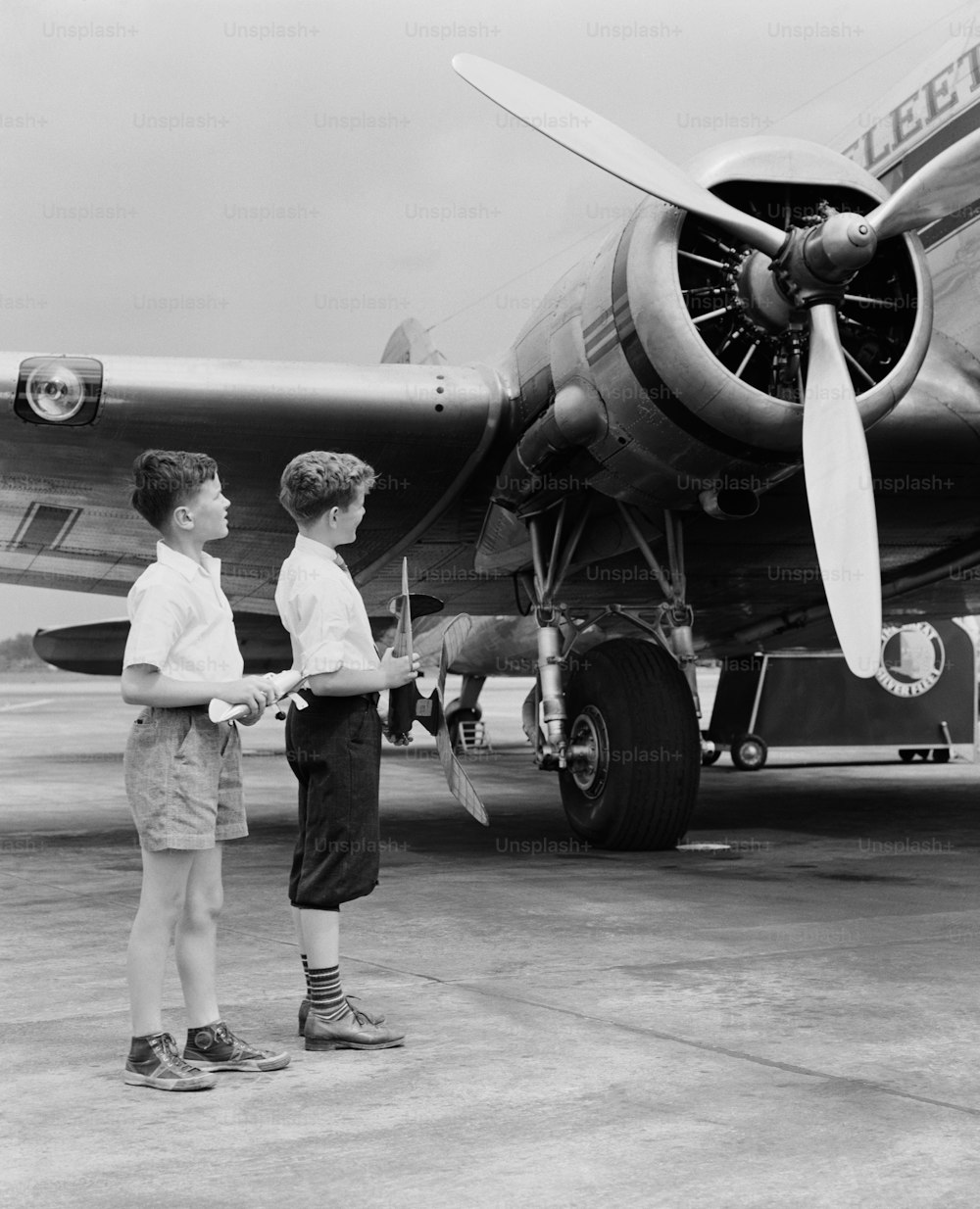UNITED STATES - CIRCA 1940s:  Two boys standing next to propeller aeroplane, holding toy plane.
