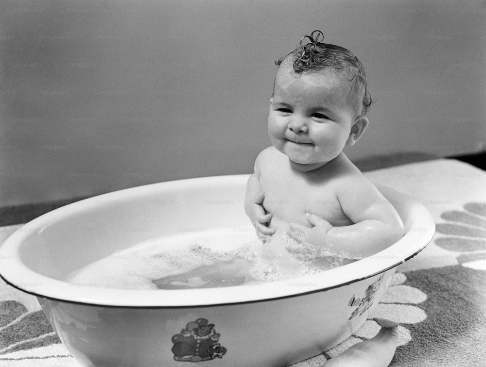 UNITED STATES - CIRCA 1940s:  Baby sitting in bath, smiling.