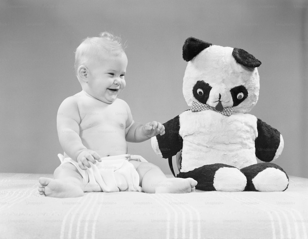 アメリカ合衆国 - 1950年代頃:パンダのぬ��いぐるみの隣に座り、笑顔で笑う赤ちゃん。