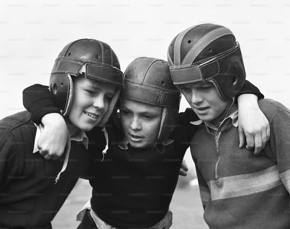 UNITED STATES - CIRCA 1950s:  Three boys wearing American football helmets, huddling together.
