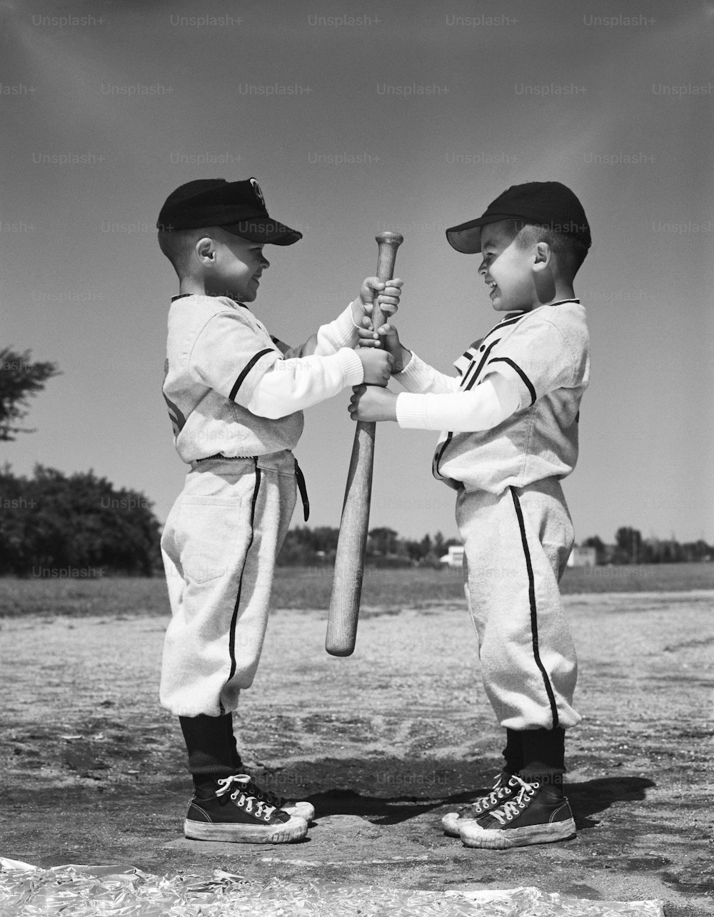アメリカ合衆国 - 1960年代頃:リトルリーグのユニフォームを着た2人の少年が、野球のバットを持って向かい合っています。