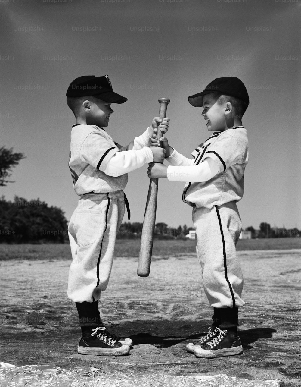 UNITED STATES - CIRCA 1960s:  Two boys in Little League uniforms, facing each other, holding baseball bat.