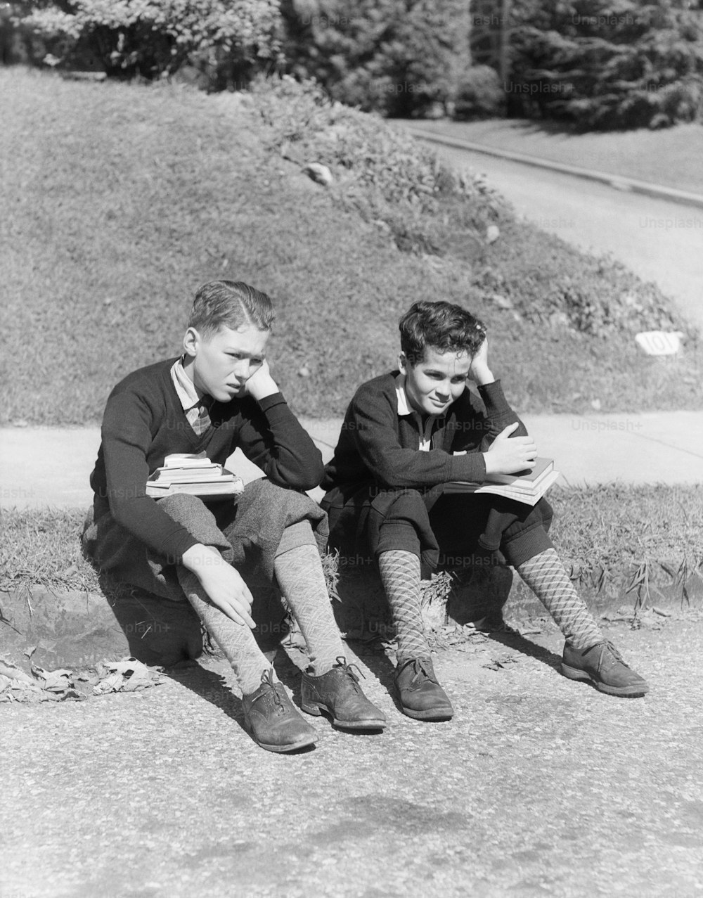 UNITED STATES - CIRCA 1930s:  Two schoolboys with books in laps, holding heads in hands.