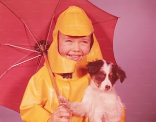 UNITED STATES - CIRCA 1960s:  Boy with umbrella, holding puppy, smiling.