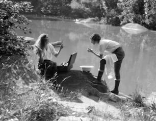 UNITED STATES - CIRCA 1930s:  Two women camping at lakeside, one combs her hair.