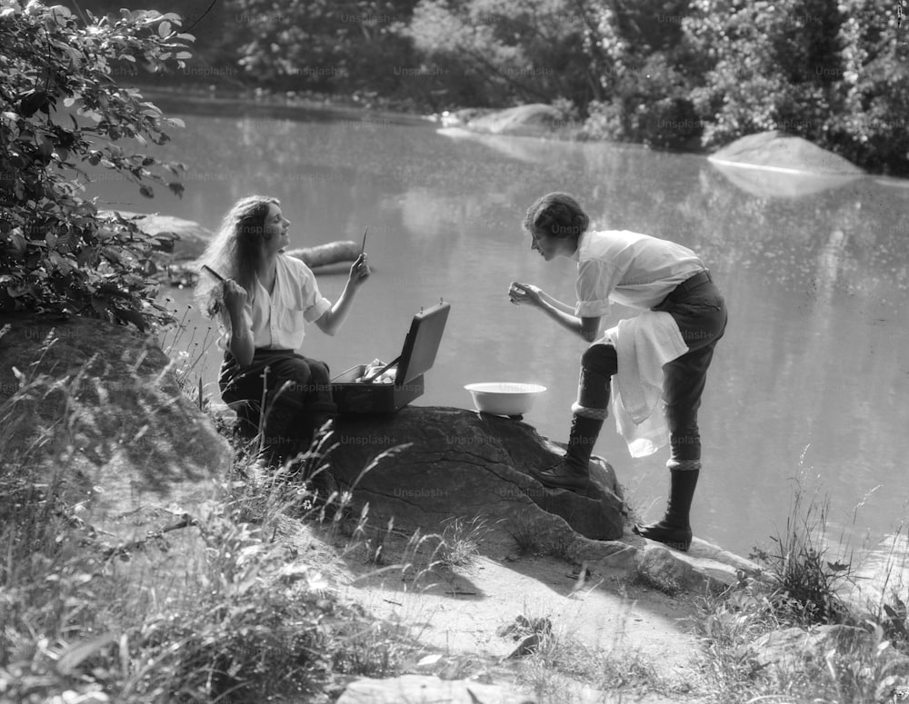 アメリカ合衆国 - 1930年代頃:湖畔でキャンプをしている2人の女性、1人が髪をとかしている。