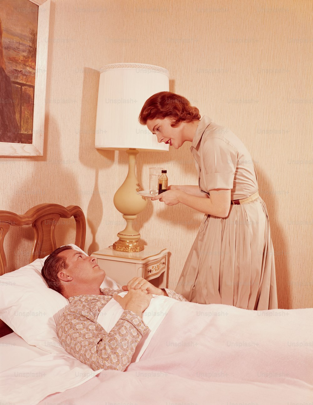 STATI UNITI - 1960 circa: Donna che trasporta vassoio di medicine al marito malato a letto.