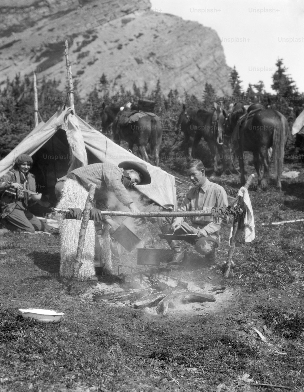 UNITED STATES - CIRCA 1930s:  Cowboy campers observe horseman cooking over fire.