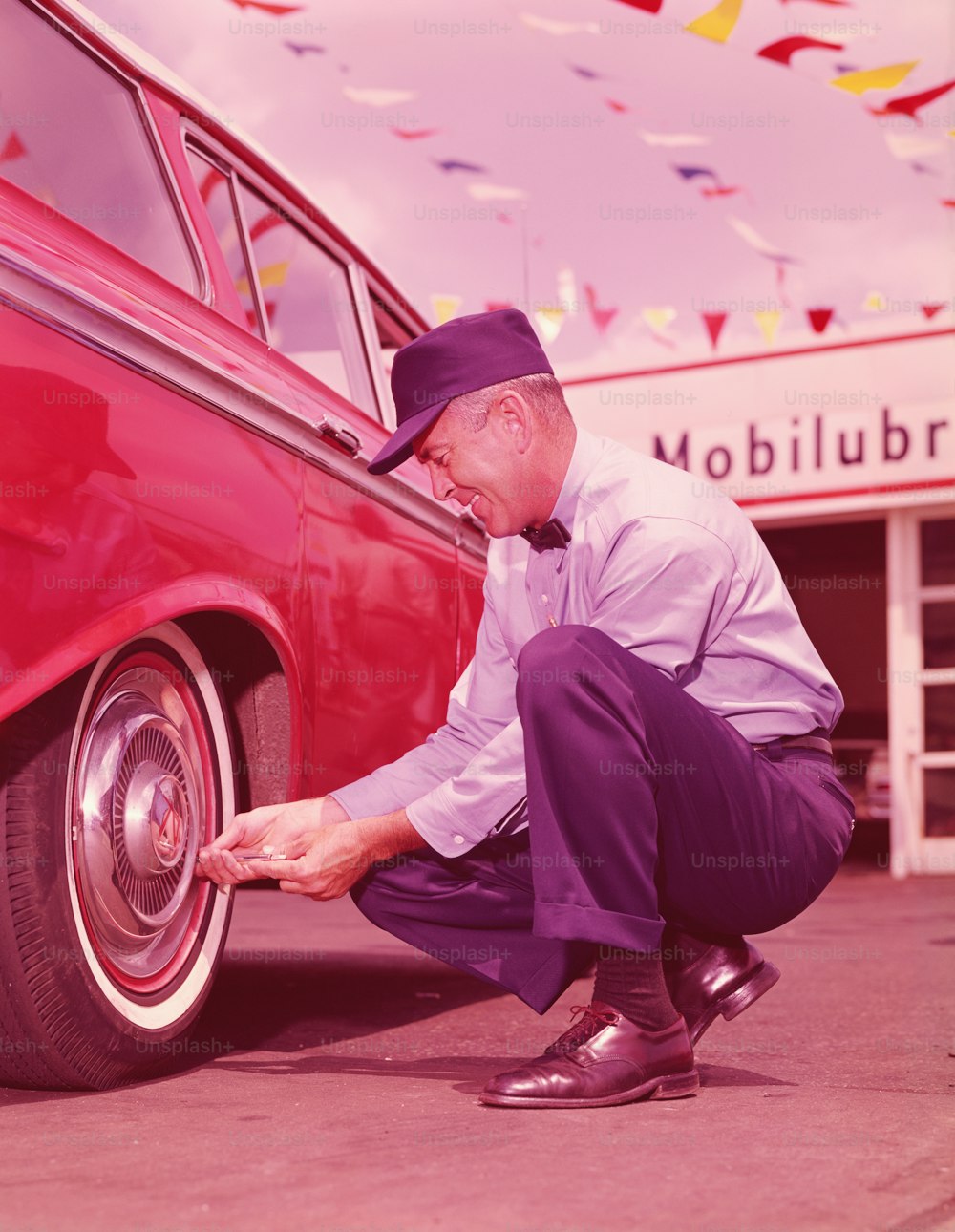 UNITED STATES - CIRCA 1960s:  Service station attendant checking air pressure in tyres of car.