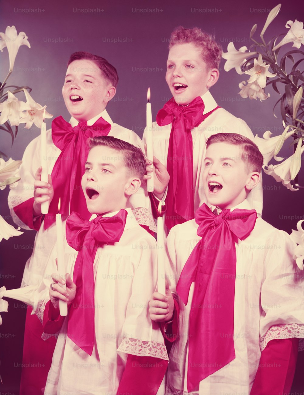 UNITED STATES - CIRCA 1950s:  Four boys in choir robes, singing, holding candles.