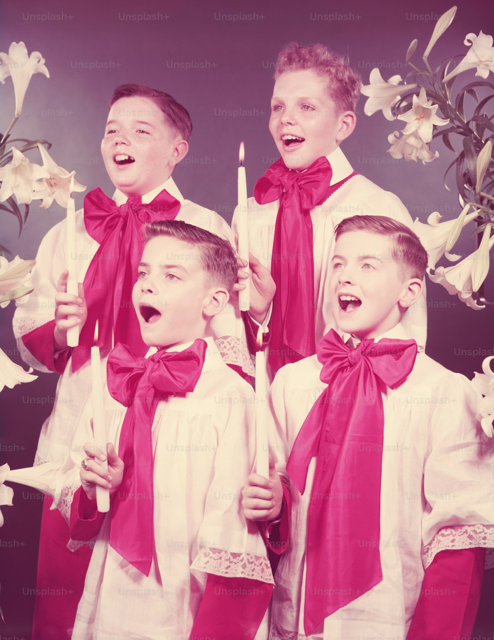 1950年代頃、聖歌隊のローブを着た4人の少年が歌い、ろうそくを手にしている。