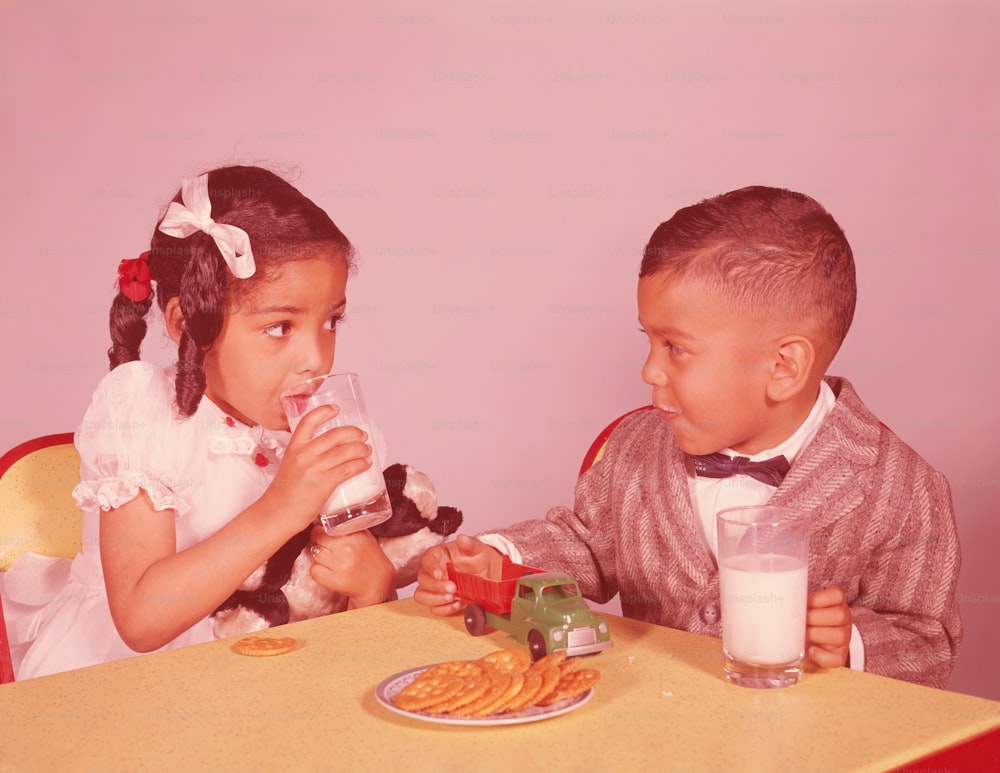 ESTADOS UNIDOS - CIRCA 1960s: Niño y niña sentados a la mesa, comiendo galletas y leche.