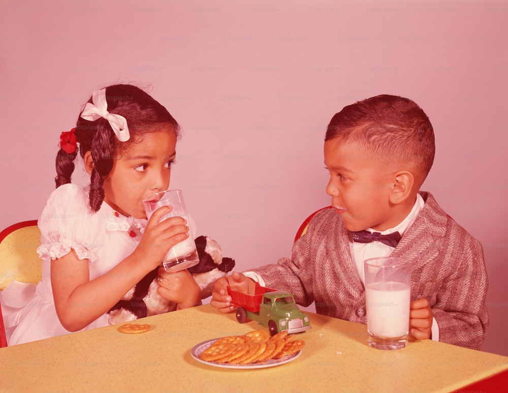 UNITED STATES - CIRCA 1960s:  Boy and girl sitting at table, having cookies and milk.