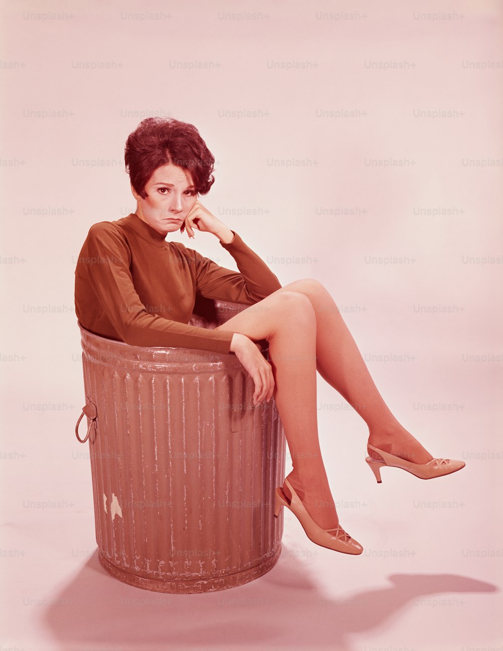 UNITED STATES - CIRCA 1960s:  Young woman in trash can with legs hanging out.