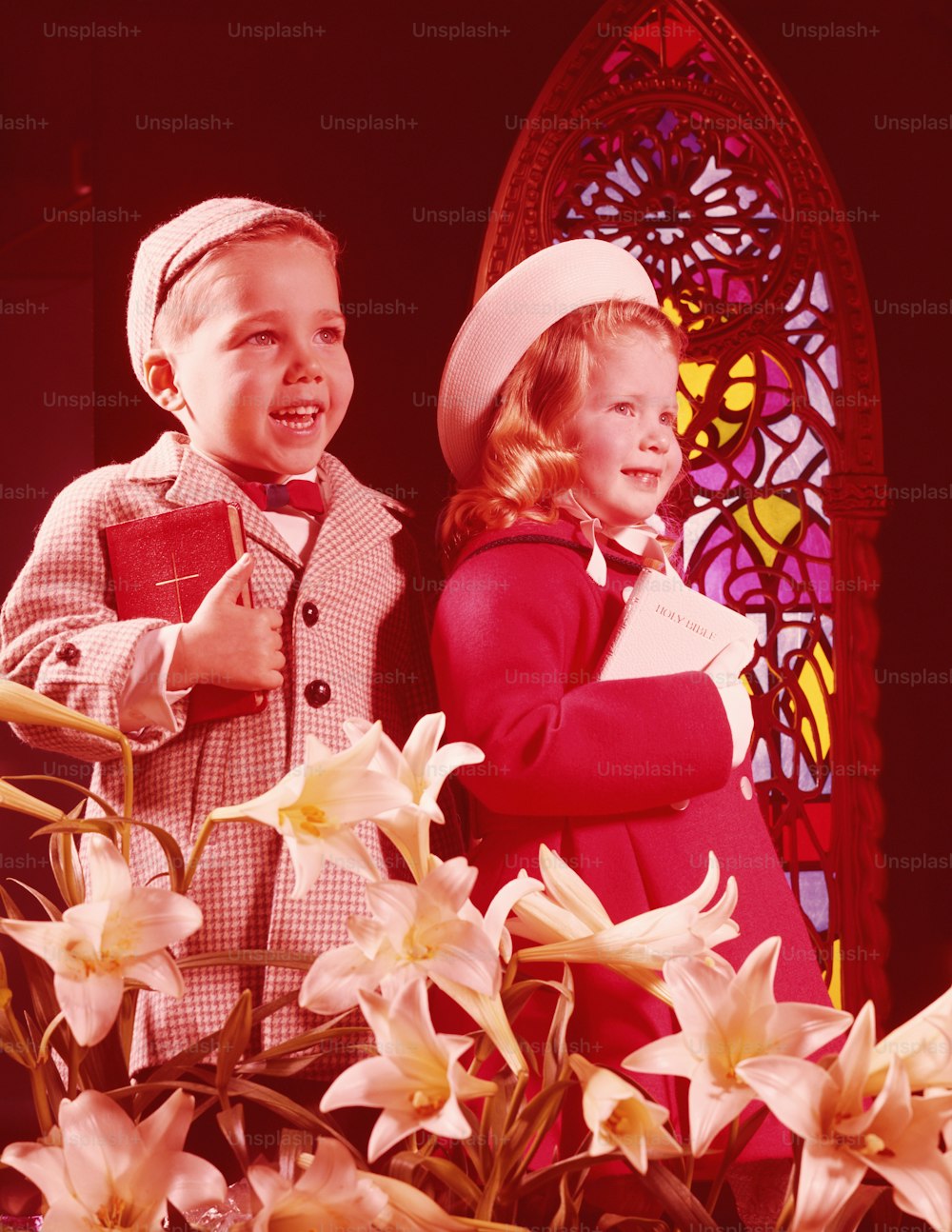 UNITED STATES - CIRCA 1960s:  Girl and boy in Sunday best, standing in front of stained glass window, lilies in foreground.