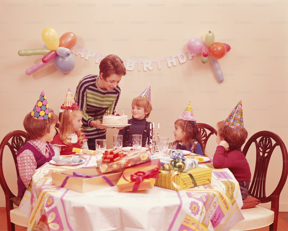 미국 - 1970년대경: 생일 파티에 참석한 다섯 명의 어린이, 생일 케이크를 제공하는 어머니.