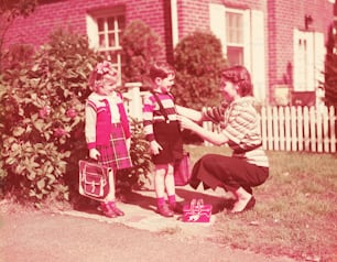 STATI UNITI - 1940 CIRCA: Madre che prepara figlia e figlio ad andare a scuola con cestini per il pranzo, libri e borse.