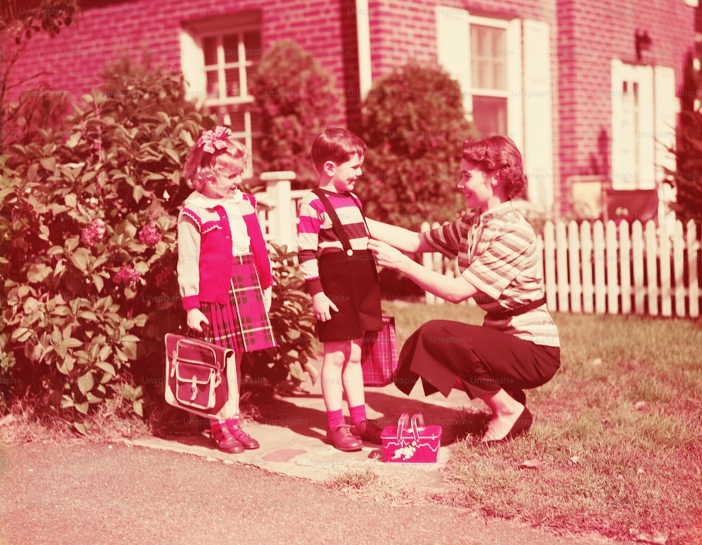 UNITED STATES - CIRCA 1940s:  Mother preparing daughter and son to go to school with lunch boxes, books and bags.