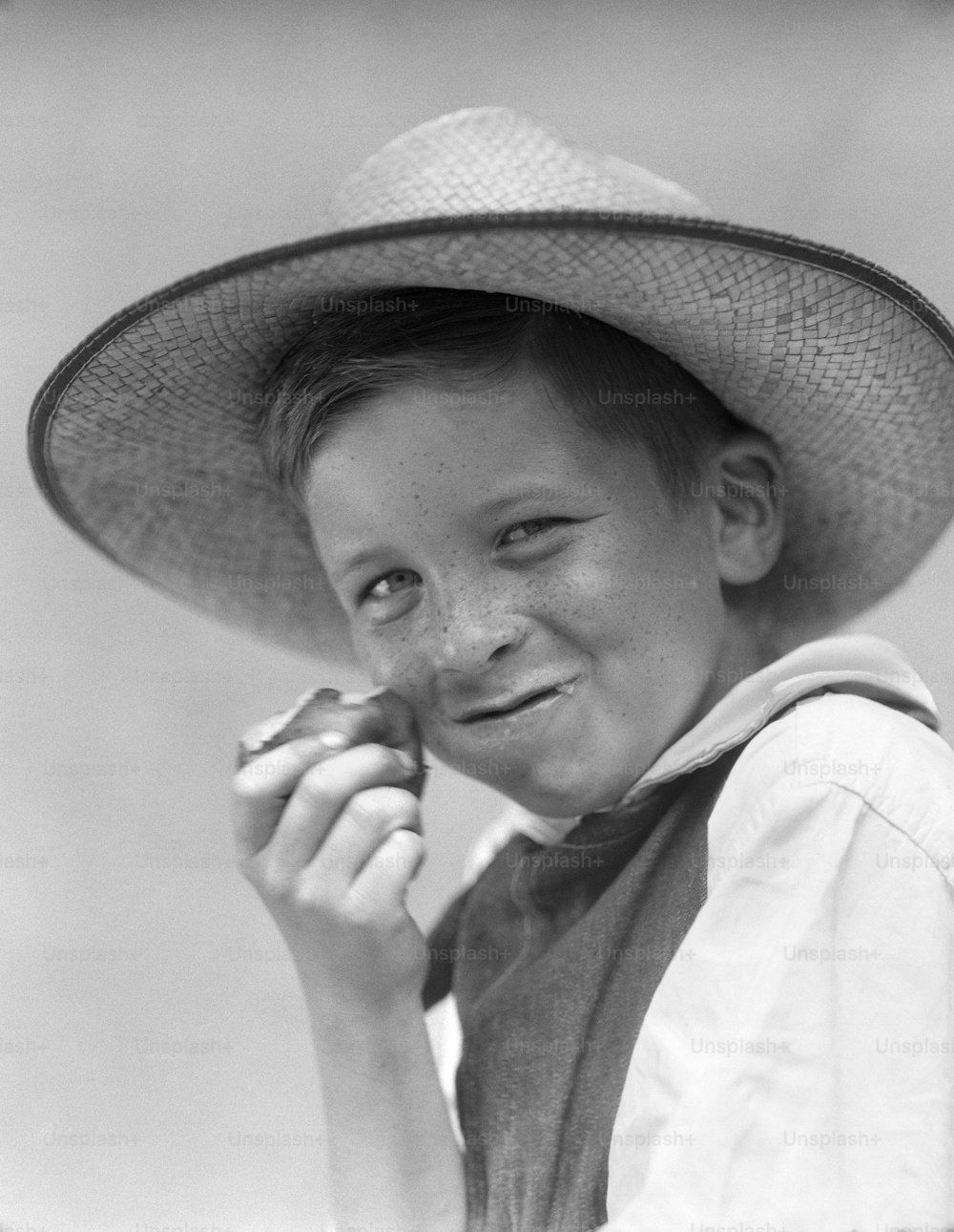 UNITED STATES - CIRCA 1930s:  Smiling boy in overalls eating an apple, mouth full.