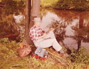 ESTADOS UNIDOS - POR VOLTA DE 1950: Homem sentado na margem do lago, pescando.