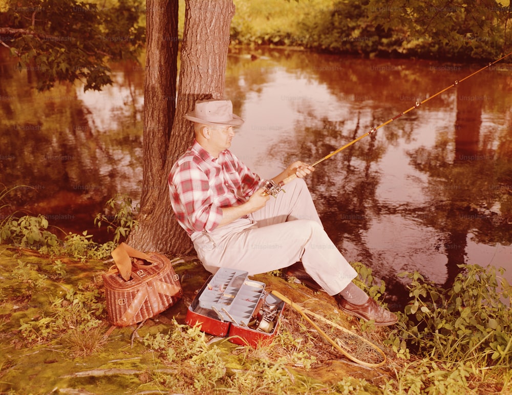 UNITED STATES - CIRCA 1950s:  Man sitting on bank of lake, fishing.