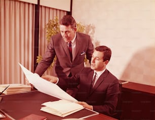 STATI UNITI - 1960 circa: due dirigenti maschi in ufficio che guardano le carte alla scrivania.