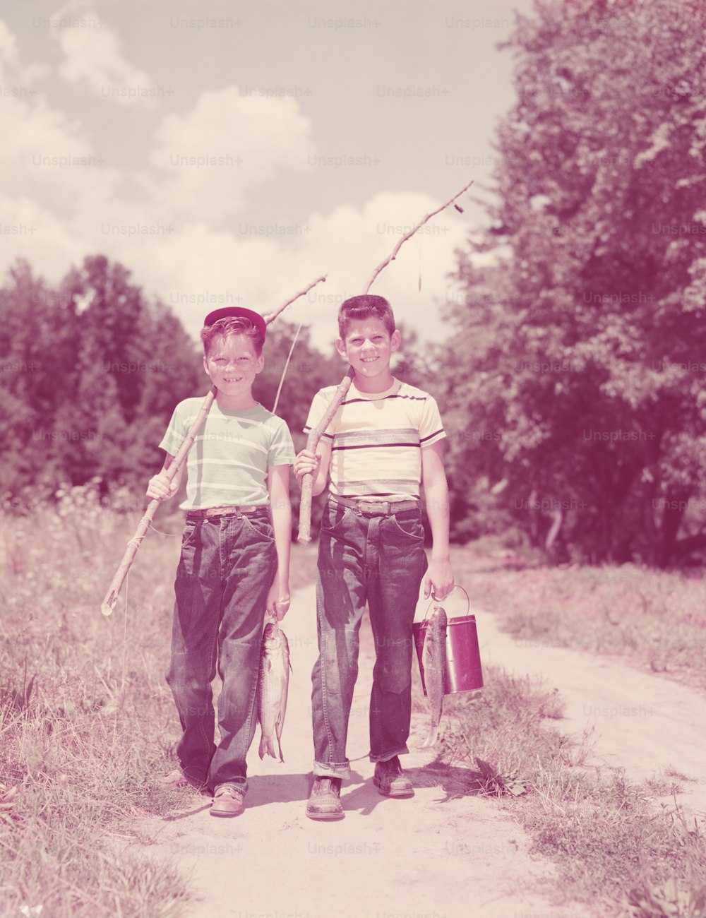 ESTADOS UNIDOS - Alrededor de la década de 1950: Dos niños caminando por la calle, cargando cañas de pescar ramitas.