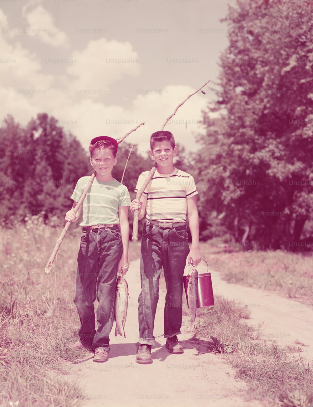 UNITED STATES - CIRCA 1950s:  Two boys walking down lane, carrying twig fishing poles.