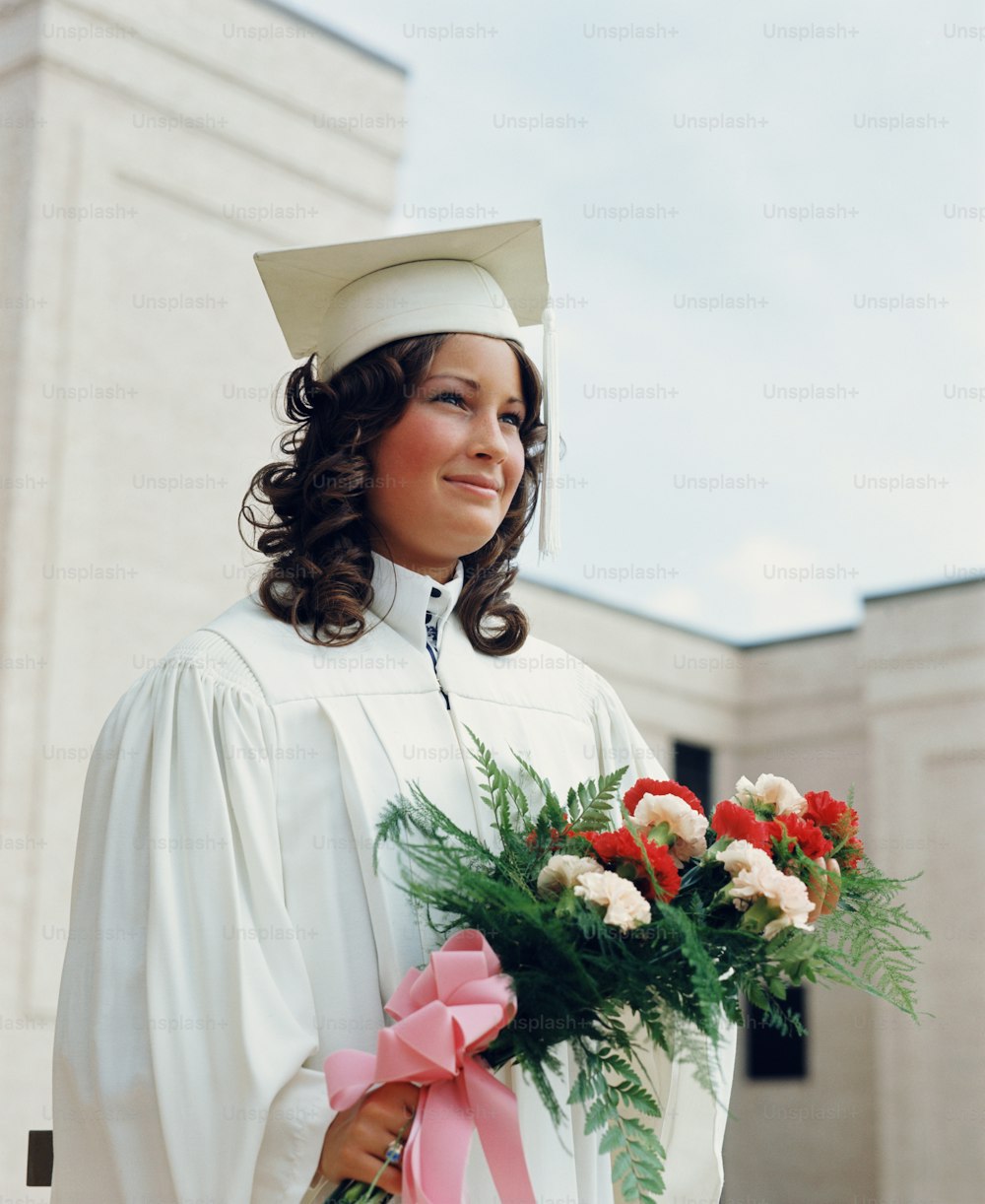 STATI UNITI - CIRCA 1970: Studente adolescente che indossa vesti bianche e mortaio, tenendo un mazzo di fiori alla laurea.