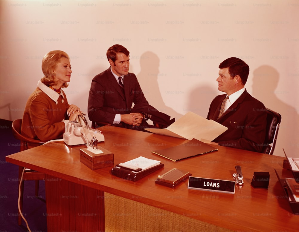 UNITED STATES - CIRCA 1970s:  Couple sitting at desk, talking to bank manager.