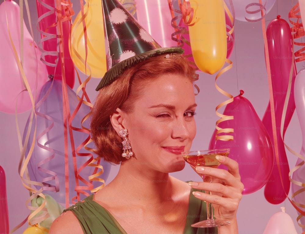 UNITED STATES - CIRCA 1960s:  Woman at party, wearing party hat and winking, holding glass of wine.