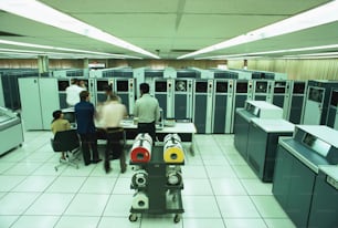 미국 - 1970년대경: 테이프 전송에 자기 테이프를 장착하는 남자, 전면에 감독 콘솔, 측면에 고속 라인 프린터.