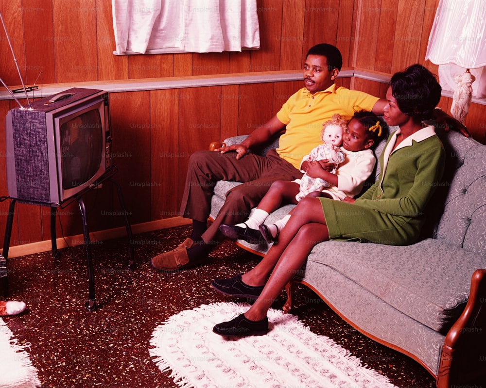 UNITED STATES - CIRCA 1970s:  Parents and young daughter sitting in living room, watching television.