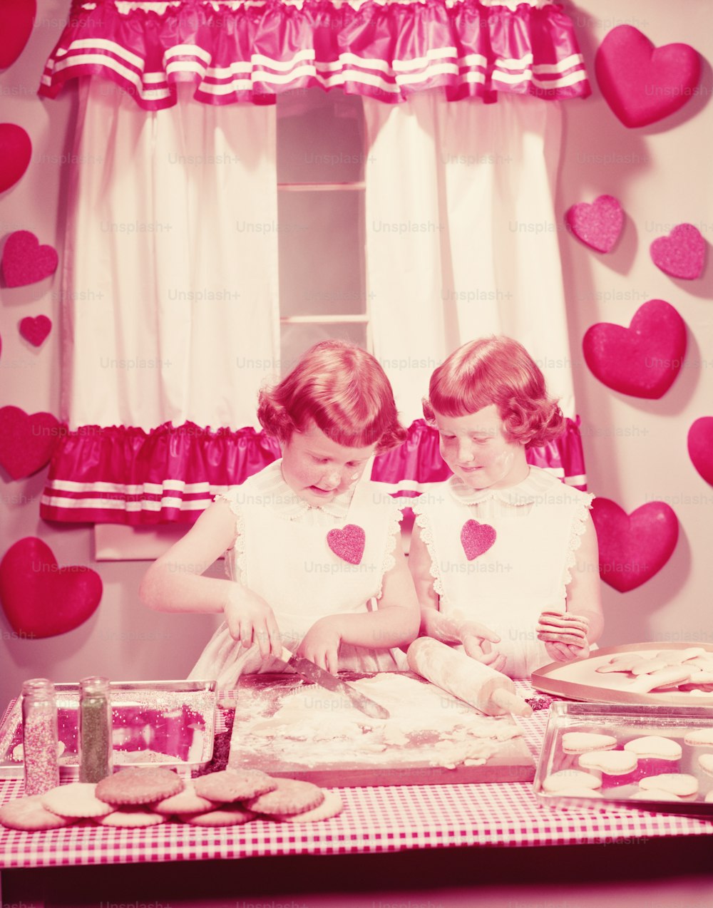 ÉTATS-UNIS - Circa 1950s : Filles jumelles dans la cuisine, préparant des biscuits de la Saint-Valentin.
