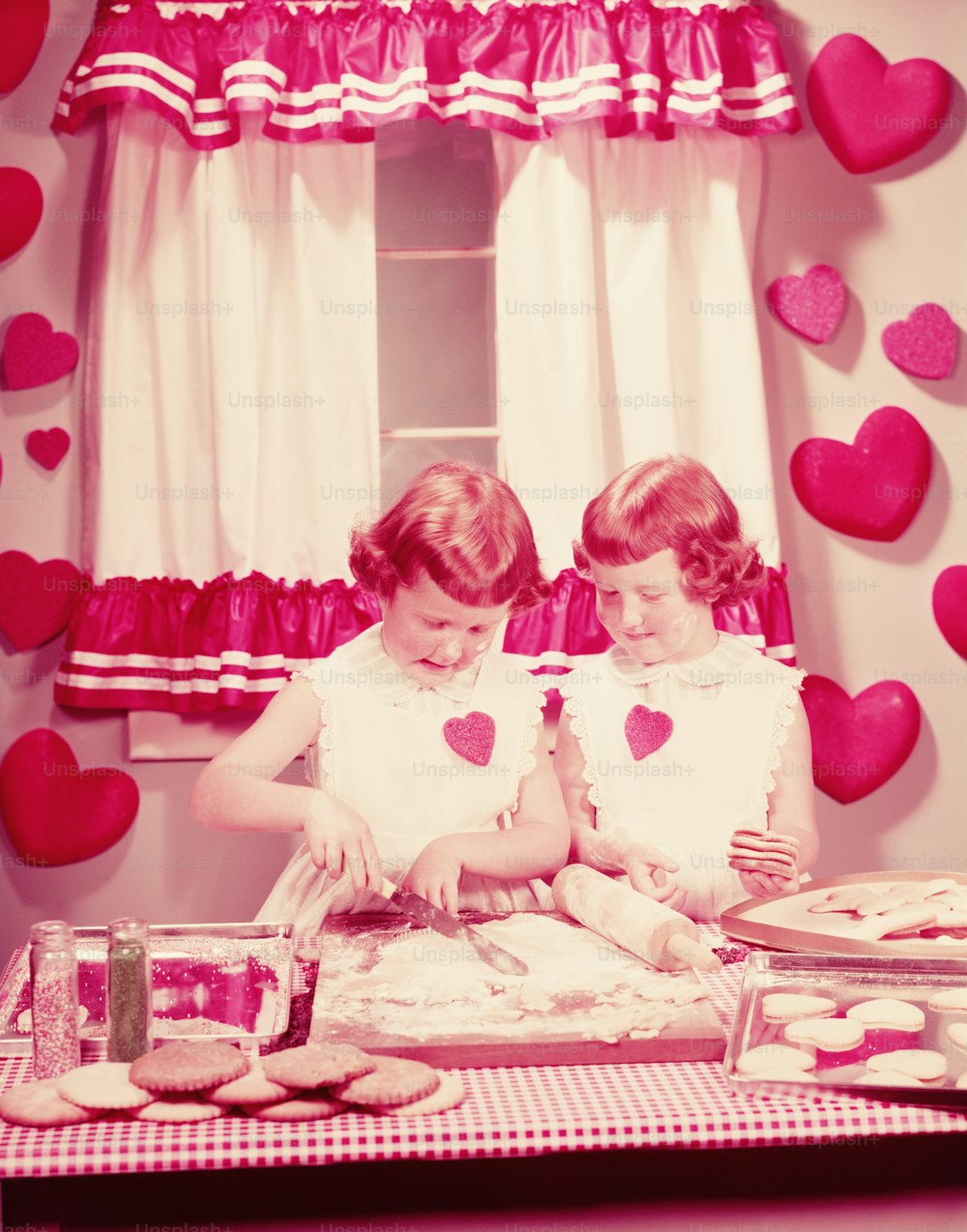 UNITED STATES - CIRCA 1950s:  Twin girls in kitchen, baking Valentine cookies.