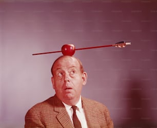 ESTADOS UNIDOS - CIRCA 1970s: Hombre de aspecto ansioso con una manzana atravesada por una flecha en equilibrio sobre su cabeza.
