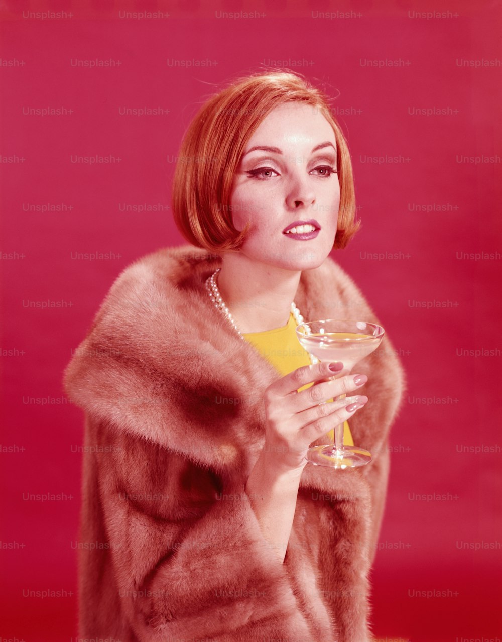 미국 - 1960년대경: 모피 코트를 입고 샴페인 잔을 들고 있는 여성.