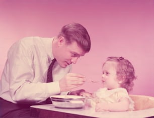VEREINIGTE STAATEN - CIRCA 1960er Jahre: Vater füttert ein kleines Mädchen, sitzt im Hochstuhl.